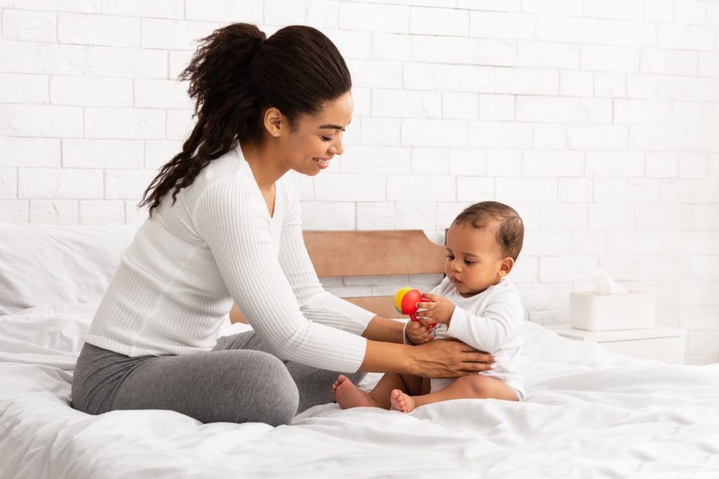 black mother playing with baby giving toy sitting in bedroom 1024x682 1